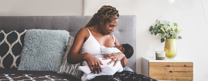 Image of mom sitting on bed and breastfeeding baby