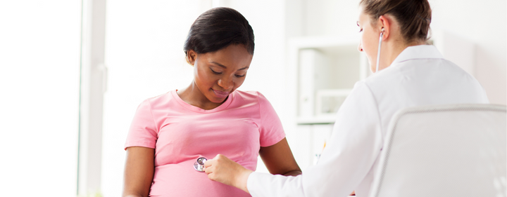 Image of a pregnant person and doctor. The doctor has a stethoscope and is resting it on the pregnant person's belly.